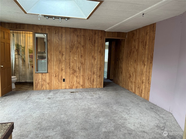 carpeted spare room with a skylight and wood walls