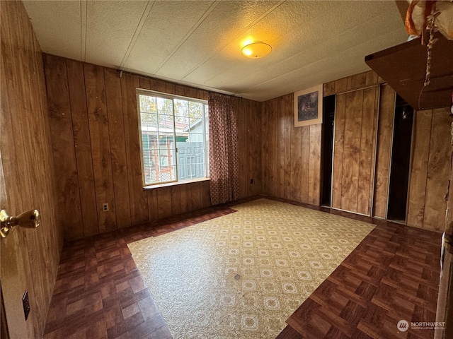 spare room with a textured ceiling, wooden walls, and dark parquet floors