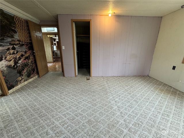 spare room featuring light carpet, wood walls, and a textured ceiling