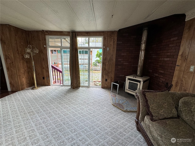 carpeted living room featuring a textured ceiling, wood walls, and a wood stove