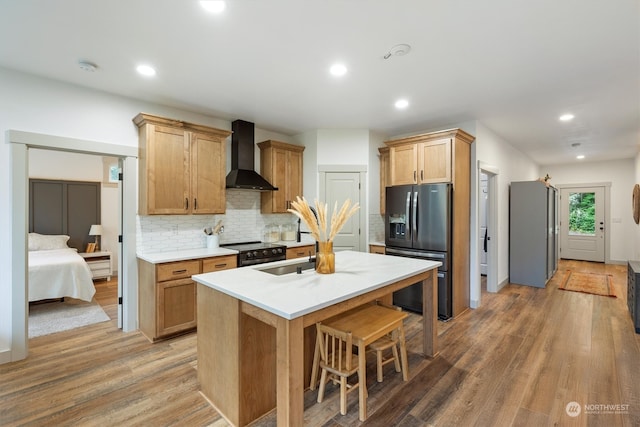 kitchen featuring black electric range oven, hardwood / wood-style flooring, wall chimney exhaust hood, a center island with sink, and refrigerator with ice dispenser