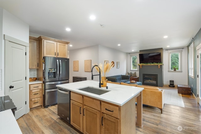 kitchen featuring an island with sink, stainless steel appliances, sink, light hardwood / wood-style floors, and tasteful backsplash