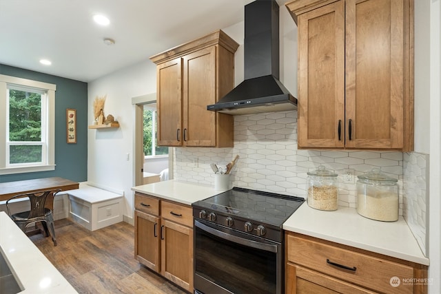 kitchen featuring wall chimney exhaust hood, hardwood / wood-style floors, tasteful backsplash, and stainless steel stove