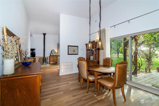 dining space with hardwood / wood-style floors, a wood stove, and a towering ceiling