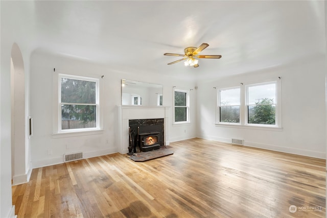 unfurnished living room with ceiling fan, a wood stove, and light wood-type flooring