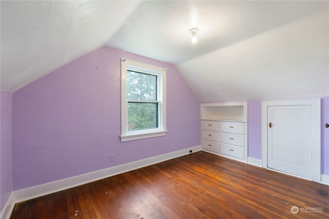 additional living space with dark hardwood / wood-style flooring, vaulted ceiling, and a textured ceiling