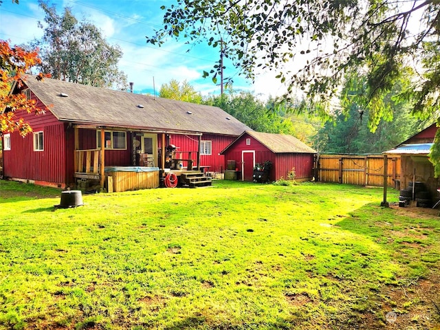 back of house featuring an outbuilding, a fenced backyard, a lawn, a hot tub, and a storage unit