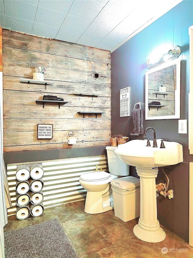bathroom featuring toilet, a sink, stone finish floor, and wood walls