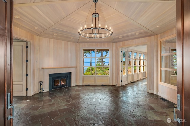 unfurnished living room featuring wooden walls, a chandelier, wood ceiling, and a raised ceiling