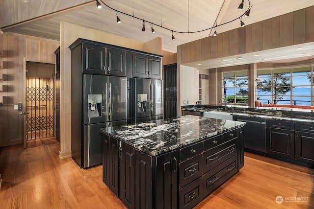 kitchen with light wood-type flooring, wooden walls, sink, dark stone counters, and appliances with stainless steel finishes