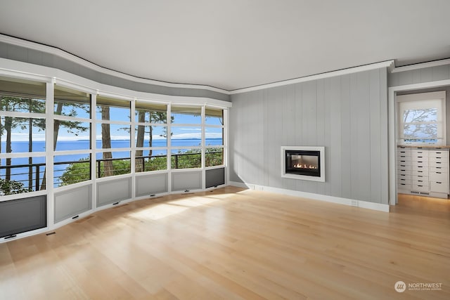 unfurnished living room featuring ornamental molding, a water view, and light wood-type flooring