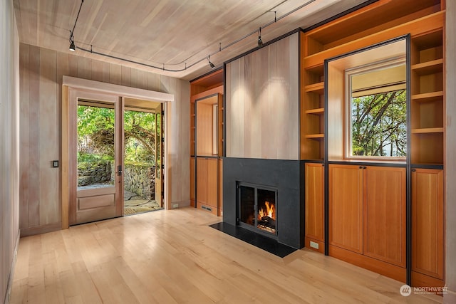 unfurnished living room featuring wooden walls, a wealth of natural light, and light hardwood / wood-style flooring