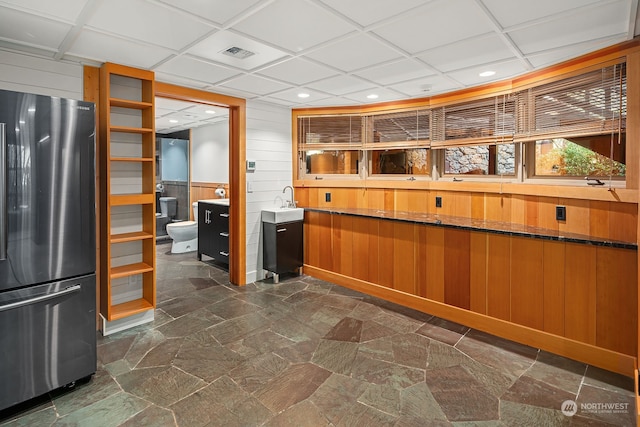 kitchen featuring wooden walls, stainless steel fridge, and a paneled ceiling