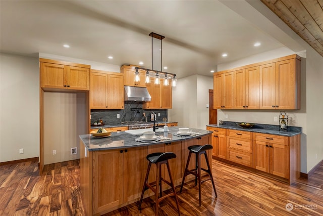 kitchen with a kitchen bar, dark wood-type flooring, sink, hanging light fixtures, and an island with sink