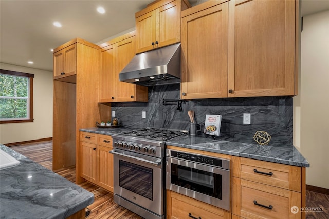 kitchen featuring decorative backsplash, appliances with stainless steel finishes, dark wood-type flooring, and dark stone counters