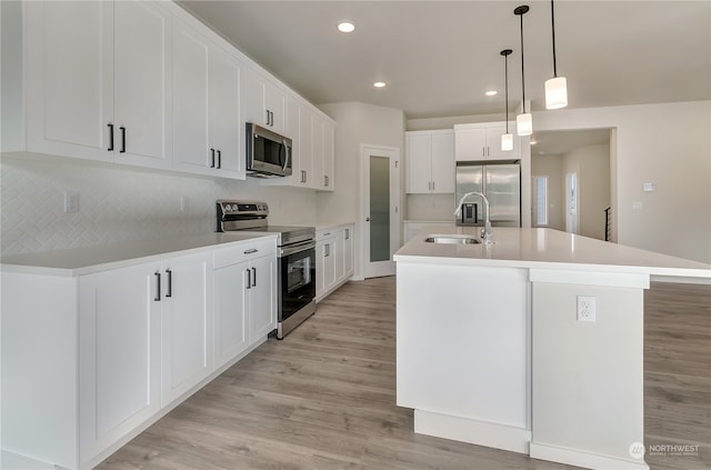 kitchen featuring white cabinets, hanging light fixtures, sink, a center island with sink, and stainless steel appliances