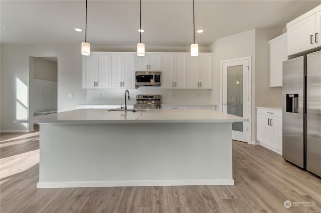 kitchen featuring an island with sink, white cabinetry, decorative light fixtures, and stainless steel appliances