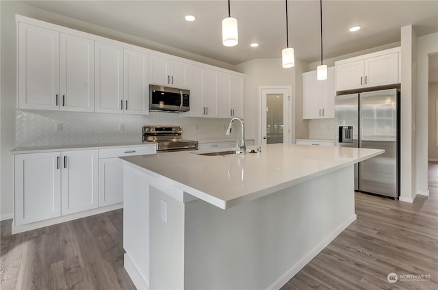 kitchen featuring a kitchen island with sink, stainless steel appliances, light wood-type flooring, and white cabinetry