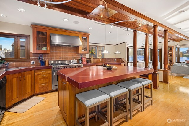 kitchen featuring high end stainless steel range, wall chimney range hood, light hardwood / wood-style flooring, and hanging light fixtures