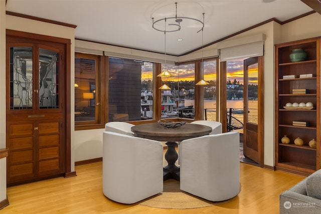 dining area with ornamental molding, light wood-type flooring, and vaulted ceiling