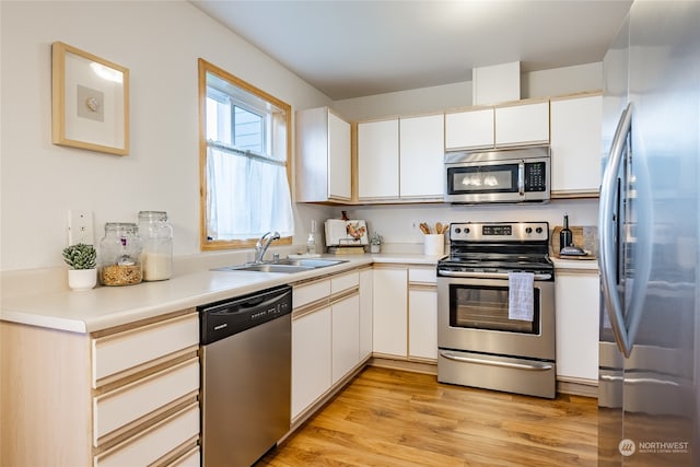 kitchen with stainless steel appliances, white cabinetry, sink, and light hardwood / wood-style floors