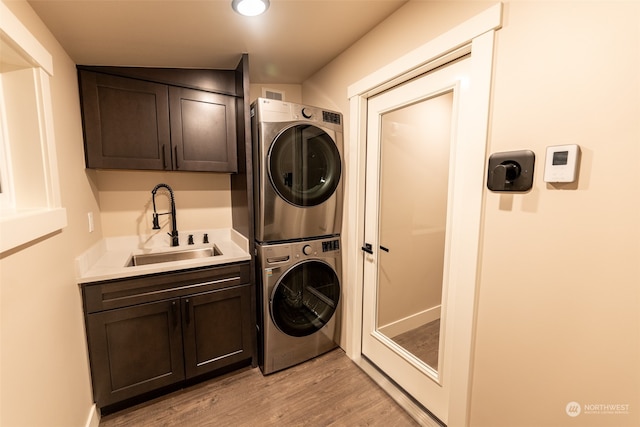 laundry area featuring cabinets, light wood-type flooring, stacked washer / dryer, and sink