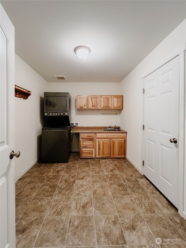 kitchen featuring a textured ceiling, stacked washing maching and dryer, sink, and black range oven