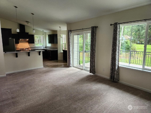 unfurnished living room featuring vaulted ceiling, dark carpet, and a healthy amount of sunlight