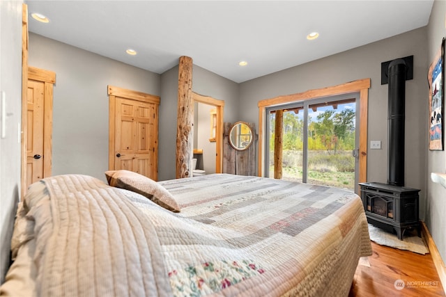 bedroom with access to outside, hardwood / wood-style floors, and a wood stove