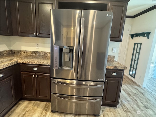 kitchen featuring crown molding, stainless steel fridge, dark stone countertops, light wood-type flooring, and dark brown cabinets