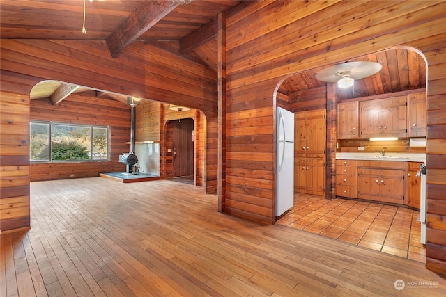 kitchen featuring light wood-type flooring, vaulted ceiling with beams, wood ceiling, a wood stove, and white fridge