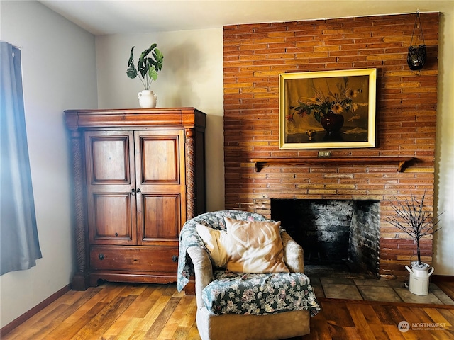 living area featuring wood-type flooring and a brick fireplace