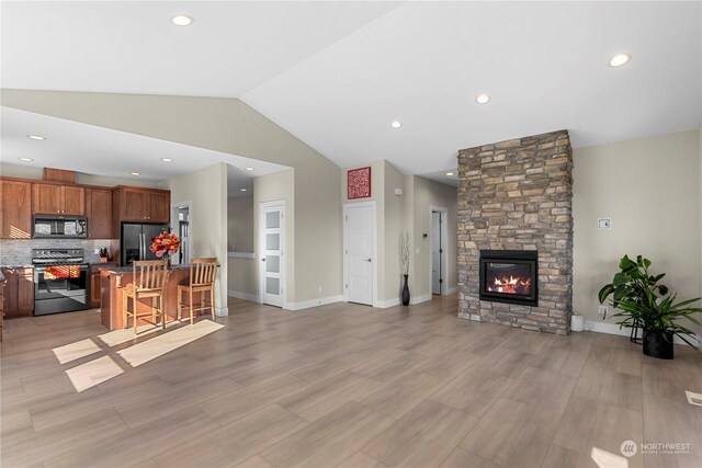 kitchen featuring a stone fireplace, decorative backsplash, a breakfast bar, a kitchen island, and appliances with stainless steel finishes