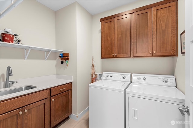 laundry room featuring washing machine and clothes dryer, sink, cabinets, and light hardwood / wood-style floors