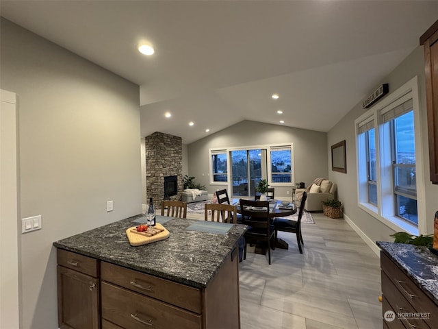 kitchen featuring a stone fireplace, dark stone counters, and lofted ceiling