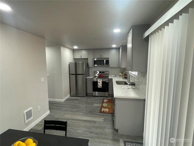 kitchen with decorative backsplash, hardwood / wood-style floors, sink, appliances with stainless steel finishes, and gray cabinets