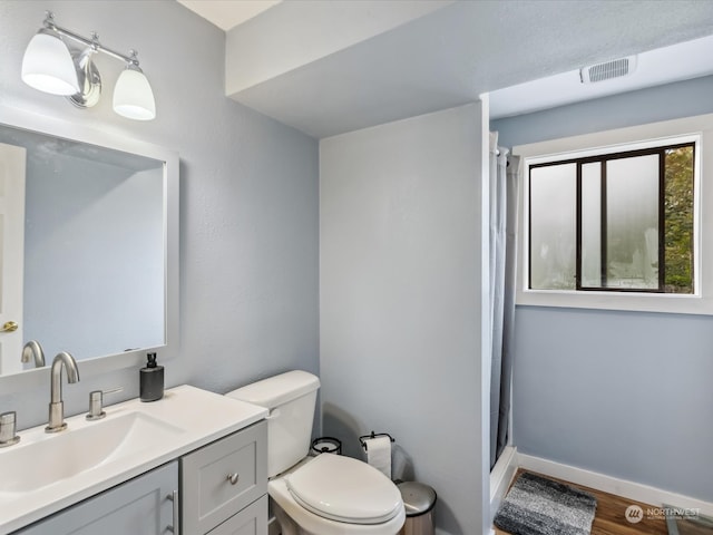 bathroom with walk in shower, hardwood / wood-style floors, vanity, and toilet