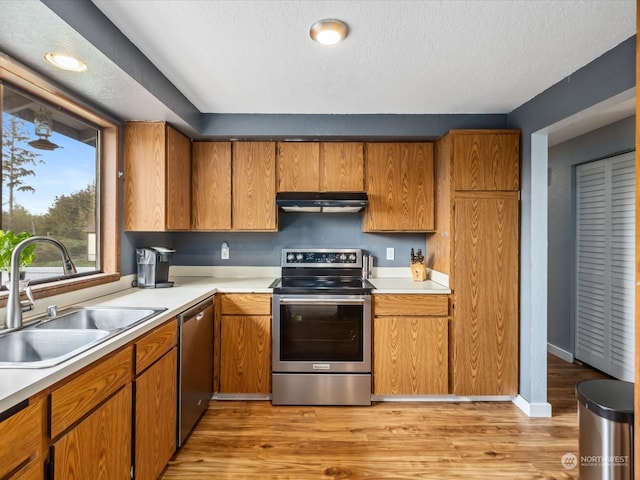 kitchen featuring appliances with stainless steel finishes, sink, light wood-type flooring, and a textured ceiling