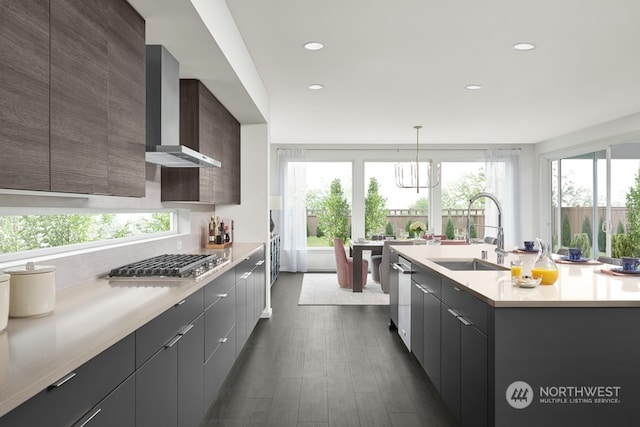 kitchen with pendant lighting, a kitchen island with sink, wall chimney range hood, appliances with stainless steel finishes, and dark hardwood / wood-style flooring