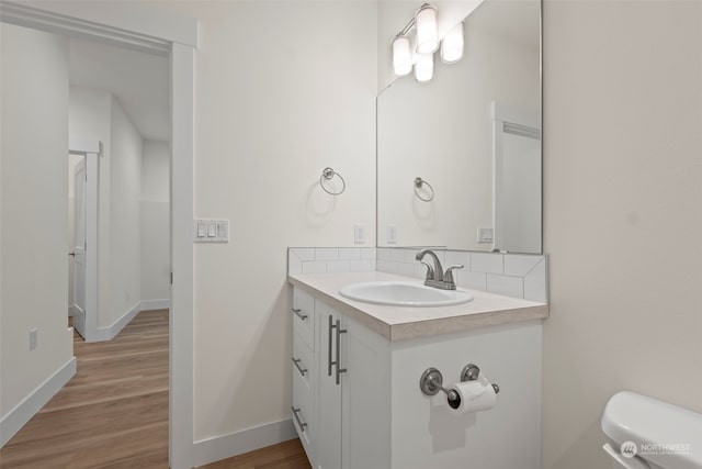 bathroom with vanity, hardwood / wood-style flooring, toilet, and decorative backsplash