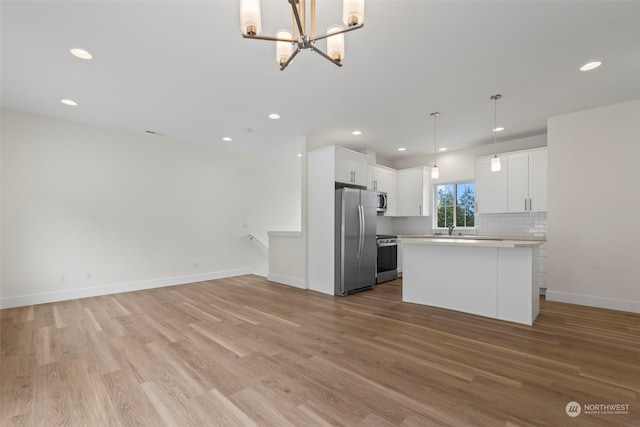 kitchen featuring white cabinets, hanging light fixtures, stainless steel appliances, a center island, and light hardwood / wood-style floors