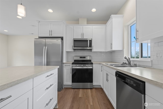 kitchen with dark wood-type flooring, sink, stainless steel appliances, hanging light fixtures, and white cabinets