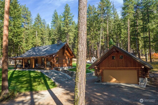 view of front of home featuring log siding, a front lawn, a porch, a chimney, and a wooded view