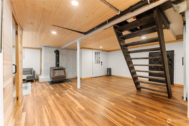 finished below grade area featuring stairway, baseboards, a wood stove, and wood finished floors