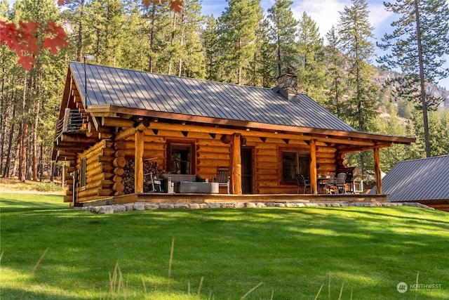 rear view of property featuring a yard, log siding, metal roof, and a chimney