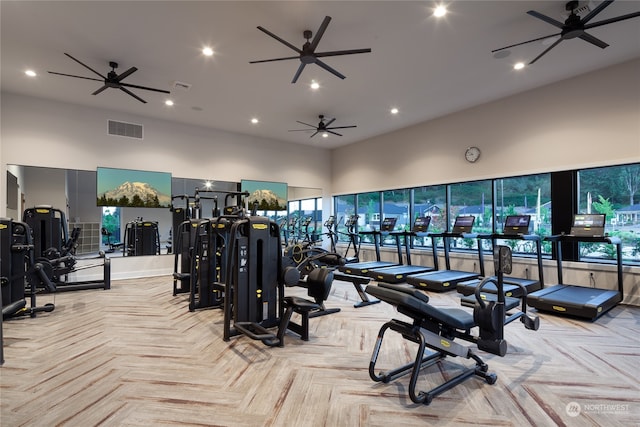 gym featuring a healthy amount of sunlight, a towering ceiling, and light parquet flooring