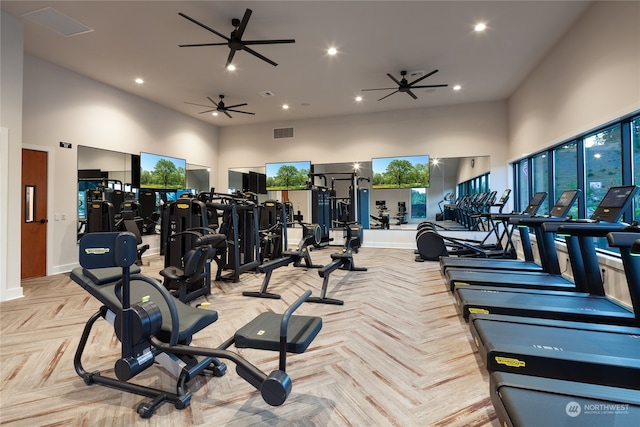 gym featuring a healthy amount of sunlight, ceiling fan, a towering ceiling, and light parquet flooring