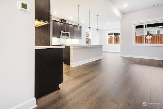 kitchen with pendant lighting, dark hardwood / wood-style flooring, decorative backsplash, a kitchen island with sink, and dark brown cabinetry