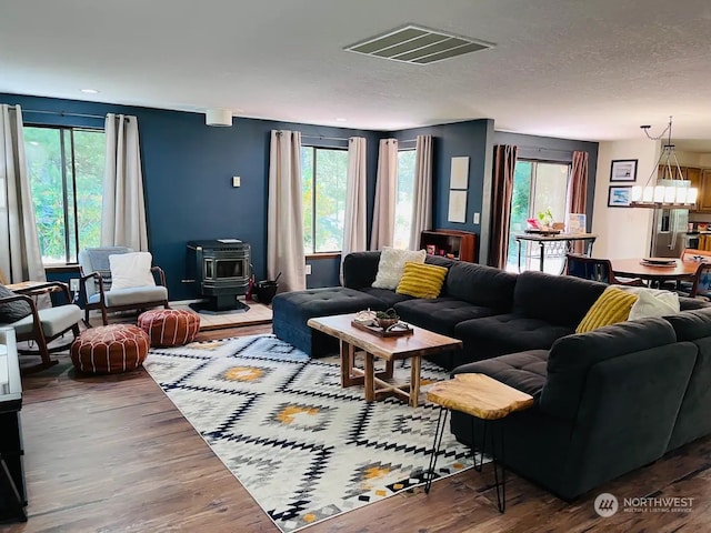 living room featuring hardwood / wood-style floors, an inviting chandelier, a textured ceiling, and a wood stove