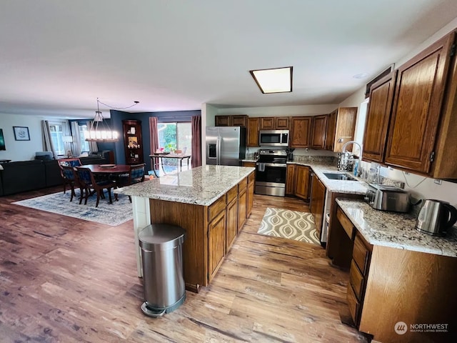 kitchen with a kitchen island, light wood-type flooring, stainless steel appliances, sink, and hanging light fixtures